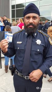 Deputy Nijjar holding up department ID at graduation.