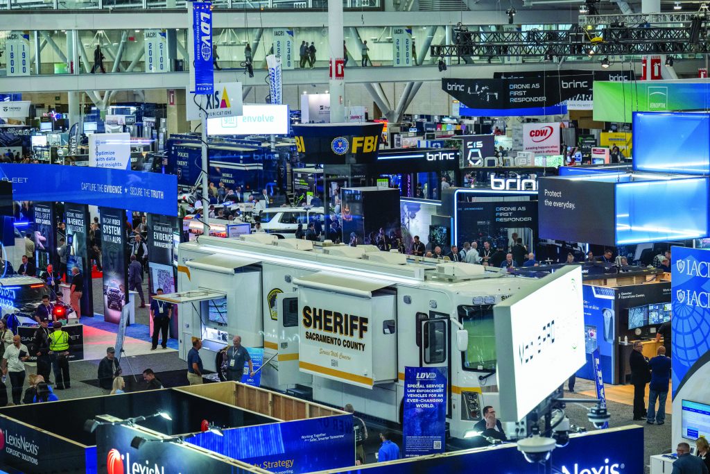 Busy law enforcement trade show with booths including FBI and tech displays; prominent 'Sheriff Sacramento County' mobile command center featured