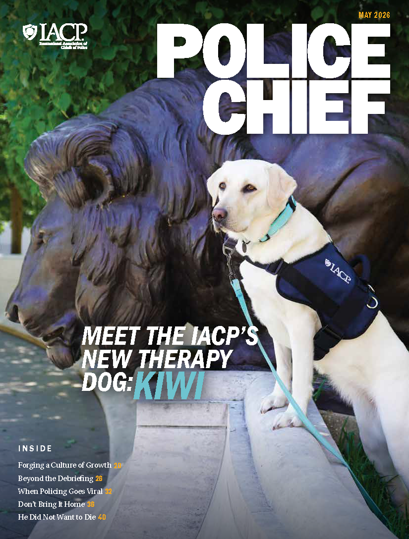 Police Chief magazine cover showing an IACP therapy dog wearing a harness beside a large stone lion statue, with bold headline text announcing the new therapy dog, Kiwi.