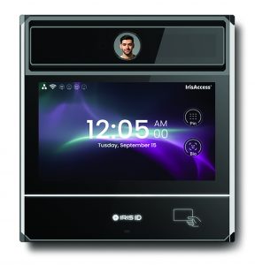 a high-tech biometric security device mounted on a wall. The device features a rectangular design with a sleek, black finish and rounded edges. At the top center of the device is an iris scanner, indicated by an icon of an eye. Below the iris scanner is a large touchscreen display showing the time "12:05 AM" and date "Tuesday, September 15." The screen also displays icons for various functions such as "Pay," "Bio," and "Settings." At the bottom center of the device is the brand name "IRIS ID" along with an icon indicating contactless card access. The overall design suggests advanced security features suitable for law enforcement or secure facilities.