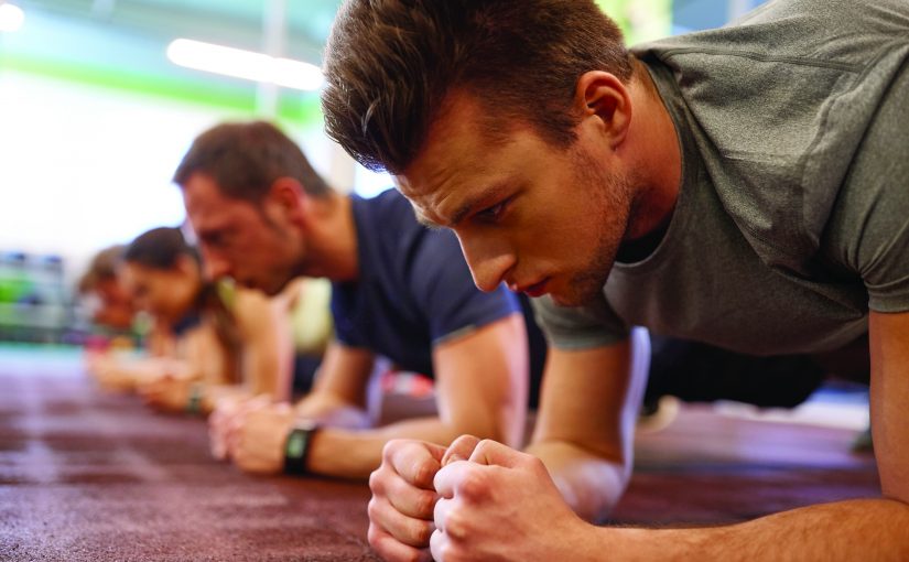 fitness, sport, exercising and people concept - close up of man doing plank exercise at group training in gym