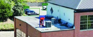 Aerial view of a brick building roof with two HVAC units; person detected holding a rifle, outlined by AI labels, with vehicles marked in green nearby.