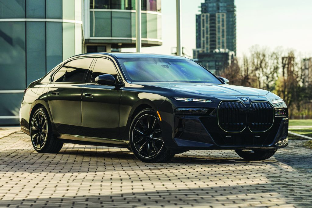 Black armored BMW sedan parked on a paved plaza, featuring reinforced body panels, bullet‑resistant glass, large grille, alloy wheels, and modern buildings in the background
