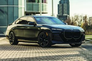 Black armored BMW sedan parked on a paved plaza, featuring reinforced body panels, bullet‑resistant glass, large grille, alloy wheels, and modern buildings in the background