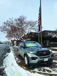 An armored SUV parked on a flat surface, designed for law enforcement use. The SUV features reinforced panels and windows, showcasing its robust and tactical design. The window has a sign providing directions to a event