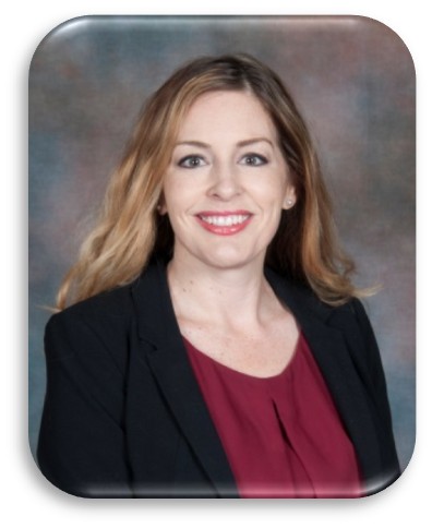 a professional portrait of an individual with long, wavy hair wearing a black blazer over a maroon blouse. The background is a gradient of muted colors, primarily consisting of shades of brown and gray. The photo has rounded corners and appears to be taken in a studio setting with soft lighting that highlights the subject's attire and hair.