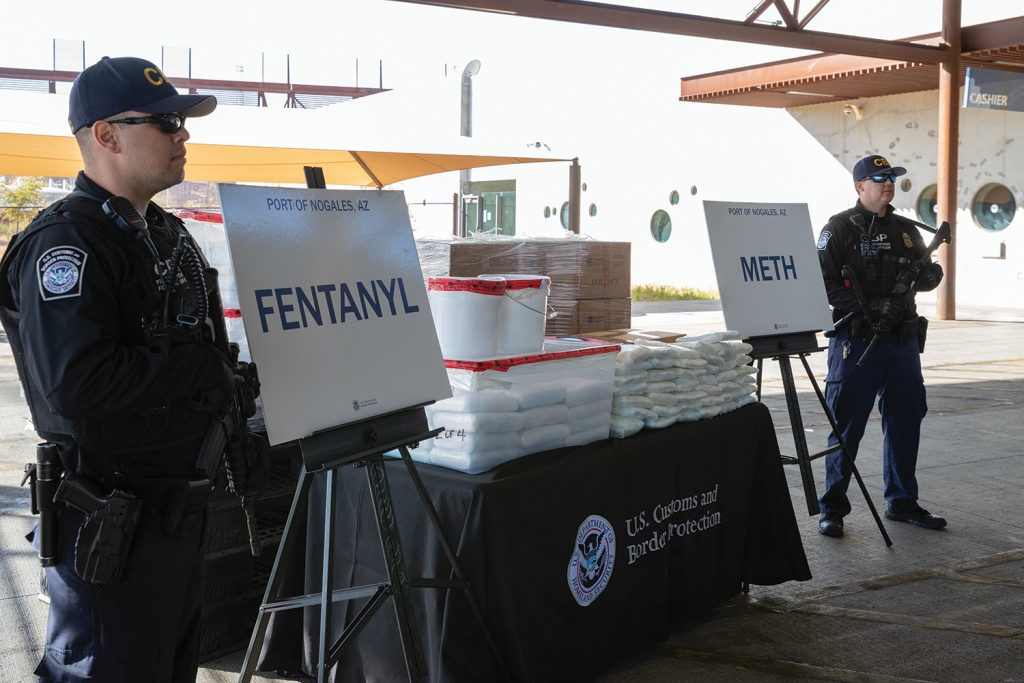CBP officers stand beside tables at Port of Nogales, AZ, displaying seized drugs labeled 'FENTANYL' and 'METH'—highlighting major narcotics interdiction