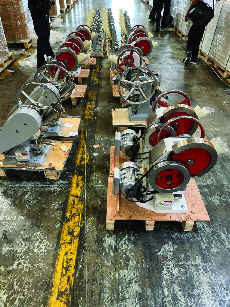 Warehouse interior with red and silver industrial machines on pallets, aligned along yellow floor lines on worn concrete—potential inspection site