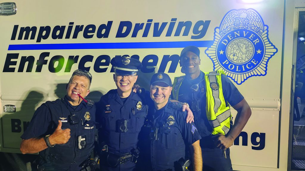 Four uniformed officers stand before Denver Police 'Impaired Driving Enforcement' vehicle; one gives thumbs up, highlighting DUI enforcement presence