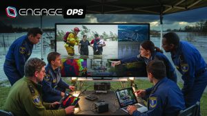 Command post under canopy shows officers reviewing flood response on large monitor with rescue footage, maps, graphs, laptops, tablets, cables, and standing water