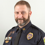 Uniformed officer; visible badge, nameplate, medals, and insignia on left chest and shoulder; attire denotes rank and service