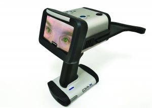 Handheld DAX Evidence Recorder captures close-up eye imagery during a sobriety assessment, with live display screen, alignment arm, examiner’s hand, classroom tables, chairs, and equipment visible
