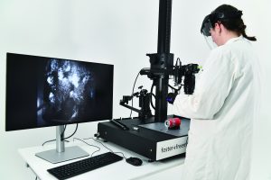 Person in lab coat uses Foster+Freeman forensic imaging device; monitor displays fingerprint image; setup supports detailed evidence analysis