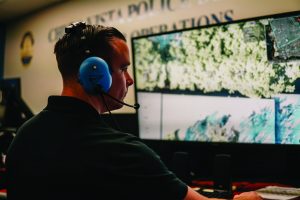 A police officer operates a drone in Arvada, Colorado, with mountains and trees on the monitor.