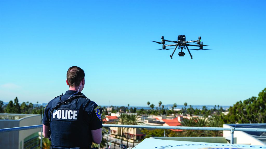 A police officer operates a drone in Colorado, with water and trees in the background.