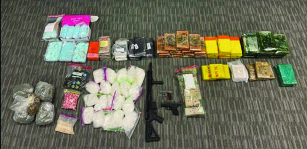Seized items on carpeted floor: packaged drugs, firearms, and stacks of cash arranged in rows and columns, documenting evidence from investigation