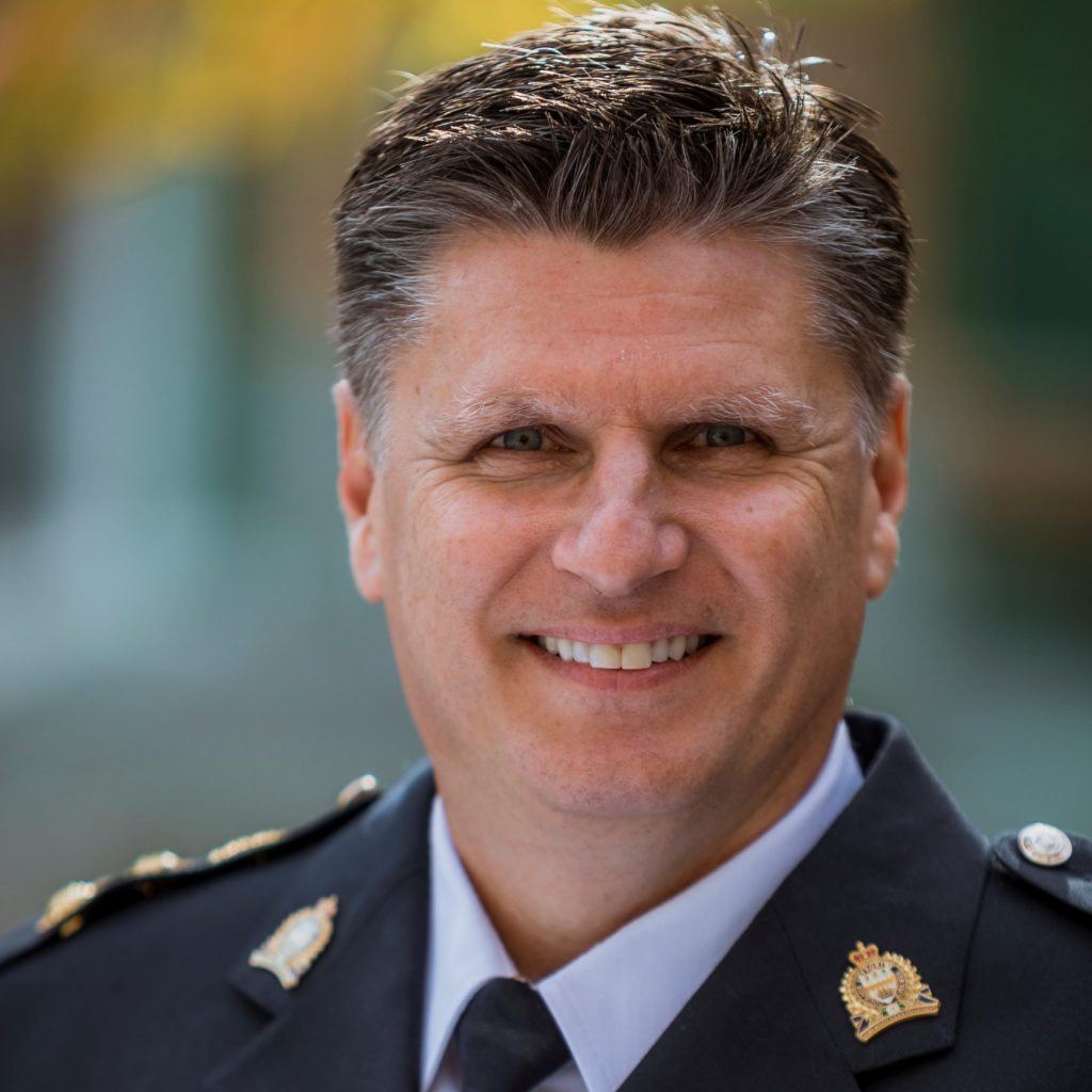 Law enforcement officer in formal uniform with shoulder epaulettes, name tag, and multiple service ribbons on left chest pocket