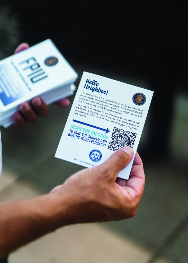 Person holds Buffalo PD flyer with QR code for feedback survey; another hand holds folded flyers labeled 'FPIU'; indoor setting