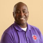 Person wearing purple polo shirt with white undershirt; shirt features red stop sign logo and text reading ‘You Can’t Stop What You Don’t Know