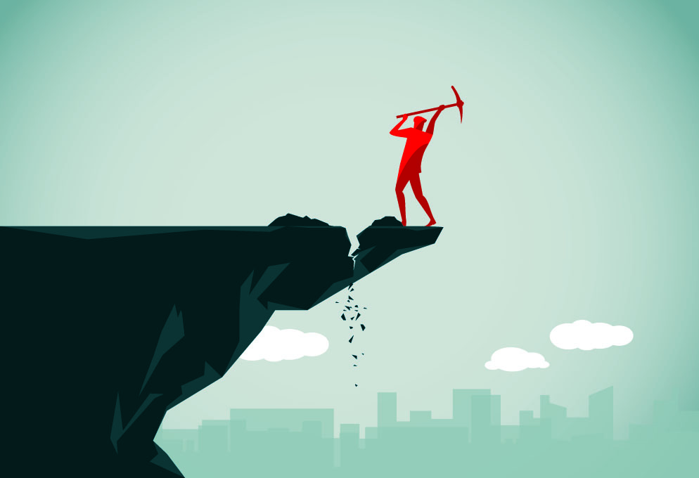 man on a cliff hacking the ground with a pick axe so the ground he is standing on will fall