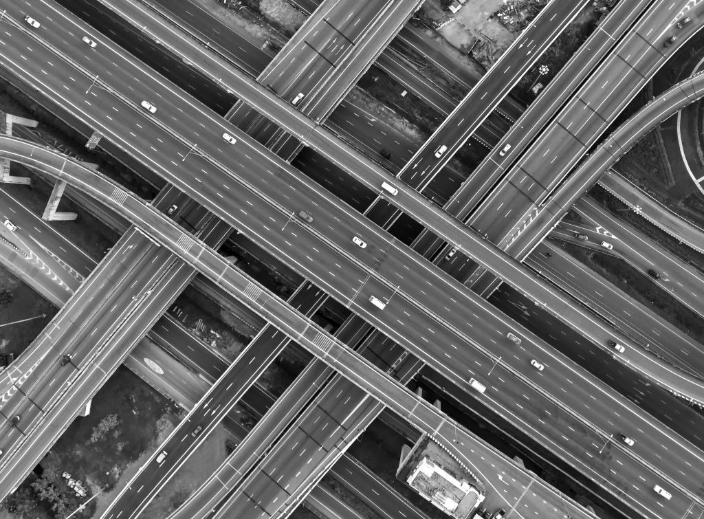 Aerial view of multi-level highway interchange with intersecting ramps and overpasses; vehicles travel in various directions across complex lanes.