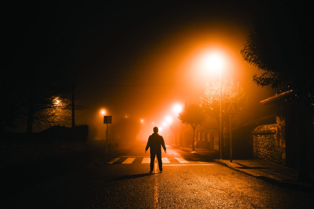 Man standing in the middle of a street at night under thick fog ...