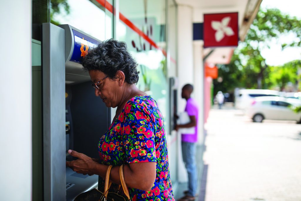 Two business‑attired figures shake hands in the foreground, overlaid with a dotted world map, with a modern city skyline and buildings visible behind