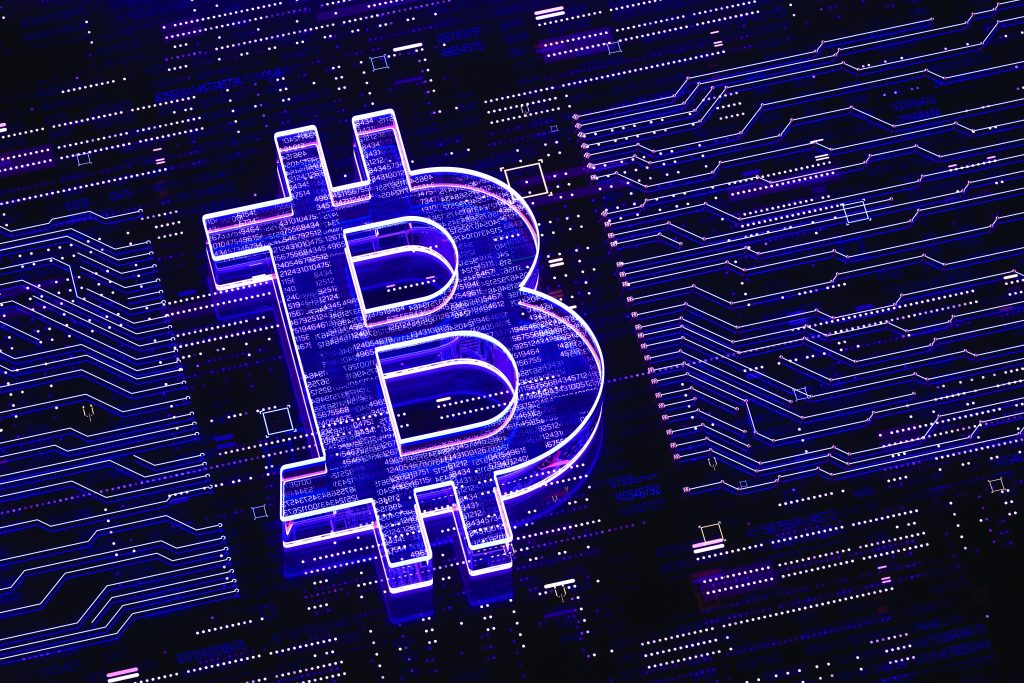 Glowing purple Bitcoin symbol appears over a dark circuit‑board background, with neon data traces, lines, and nodes suggesting cryptocurrency and digital networks