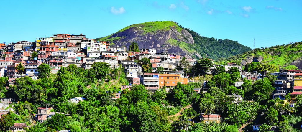 Colorful hillside homes densely packed among green trees, with large hill and clear sky in background—highlighting urban density and terrain layout