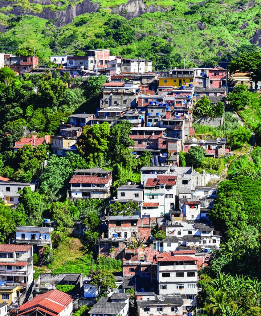 Densely packed colorful hillside homes amid lush greenery, with a rocky hilltop in back—highlighting urban density and terrain challenges