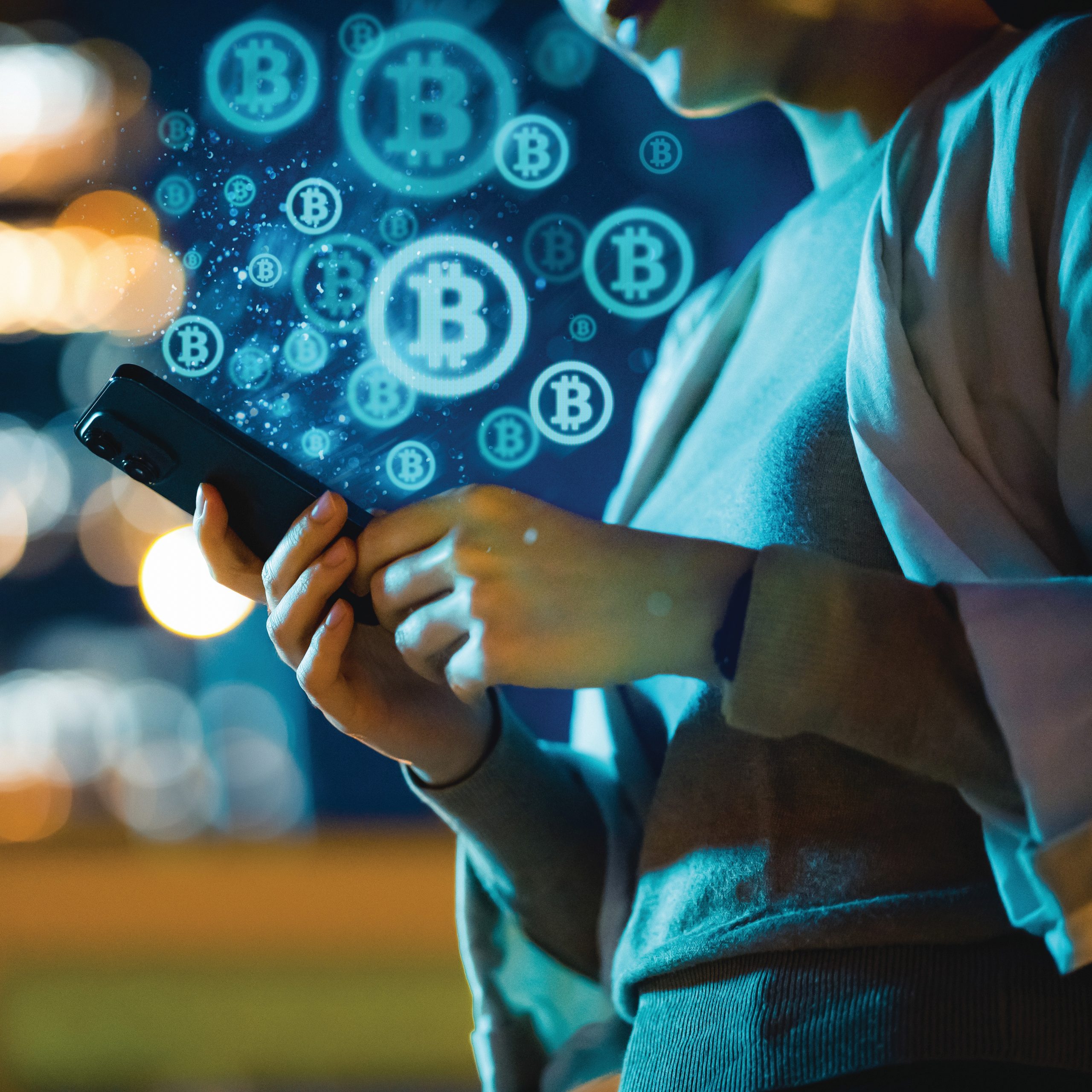 Person holds smartphone with floating Bitcoin symbols; blurred city lights in background create a night-time digital finance theme