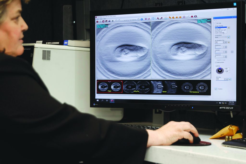 Close-up of technician’s hand using a mouse while examining detailed cartridge-case impression scans on a forensic analysis monitor beside desktop equipment