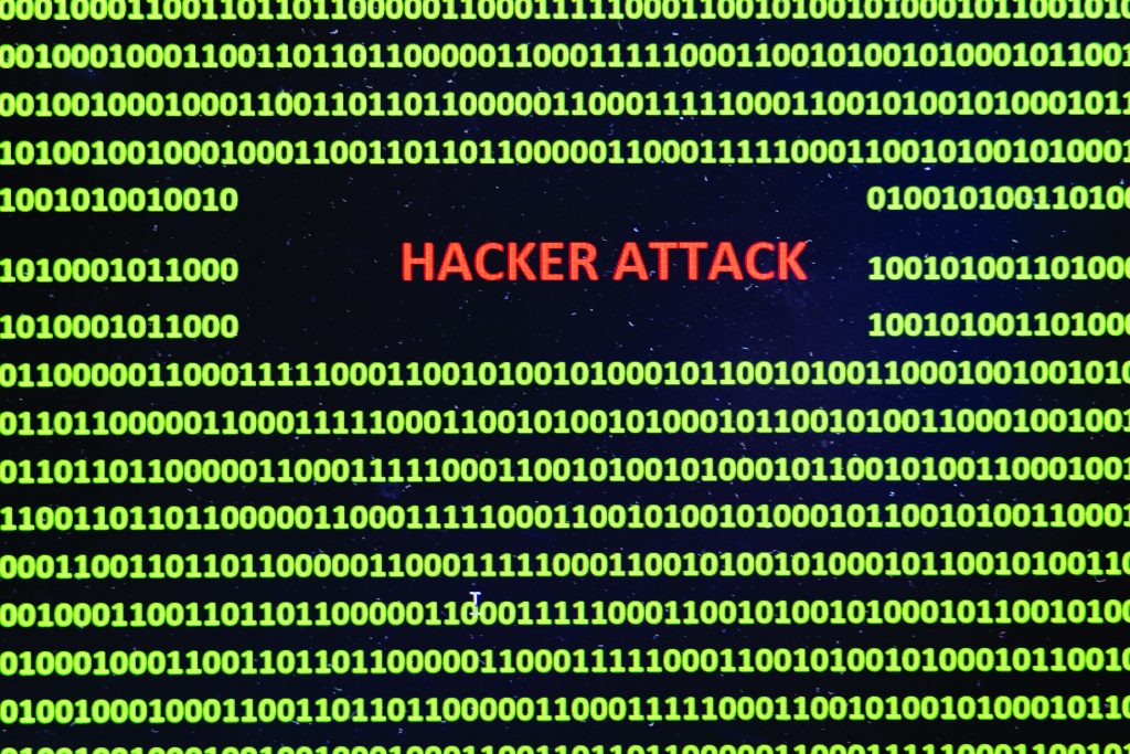 Dark background filled with green binary code rows, centered red text reading ‘HACKER ATTACK,’ suggesting a digital intrusion, cybercrime, or network security breach