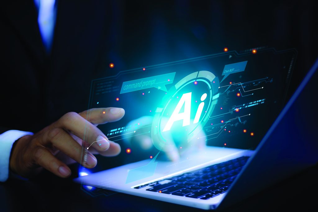 The image shows a person in a suit using a laptop. The screen displays a digital interface with the prominent letters "Ai" in the center, surrounded by various icons and graphical elements. The background is dark, highlighting the glowing blue and white interface on the screen. Small orange dots are scattered around, adding to the futuristic feel of the image.