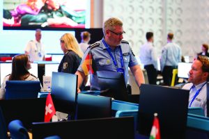 Uniformed personnel at computer stations in modern control room, with Swiss and German flags visible, highlighting international law enforcement work