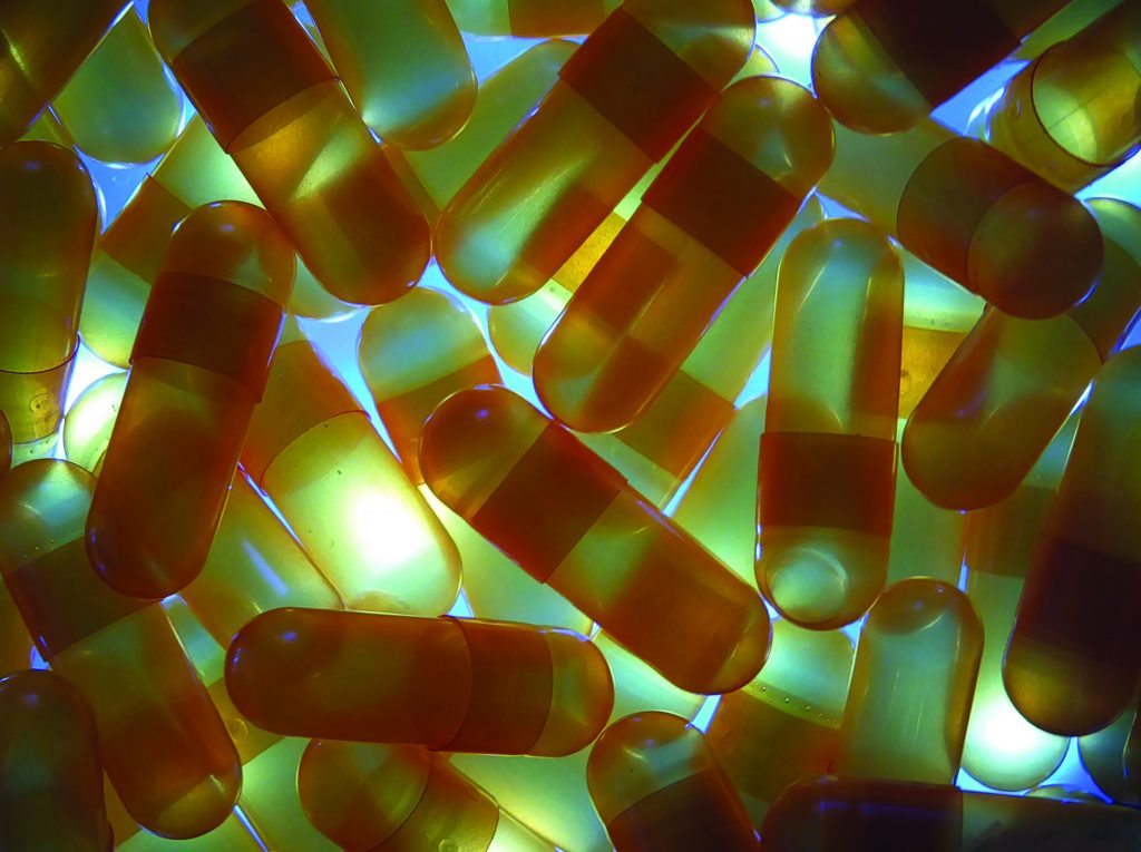 Close-up of translucent amber capsules with central seam, scattered and overlapping on blue-lit surface, suggesting pharmaceutical or illicit substances