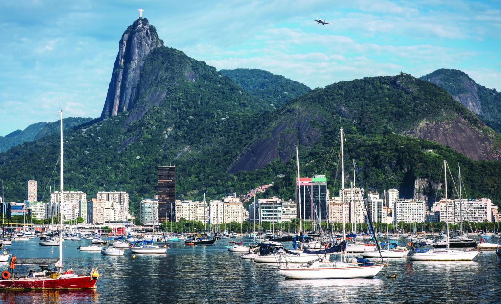 Rio de Janeiro harbor with docked sailboats, urban skyline, and Christ the Redeemer on Corcovado Mountain under clear skies, viewed from elevated angle