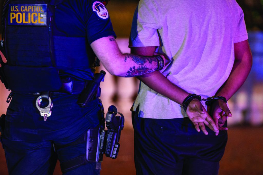 U.S. Capitol Police officer secures an individual in handcuffs, standing side by side at night with visible duty belt, holstered gear, and tactical uniform
