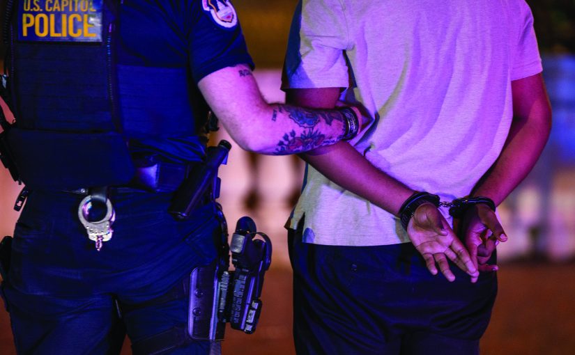 U.S. Capitol Police officer secures an individual in handcuffs, standing side by side at night with visible duty belt, holstered gear, and tactical uniform