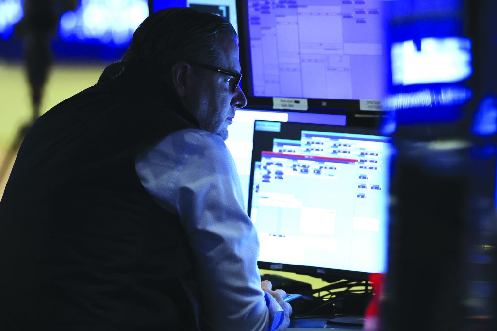 Person seated at a workstation with multiple monitors displaying complex data and schedules, working in a dimly lit control or operations environment