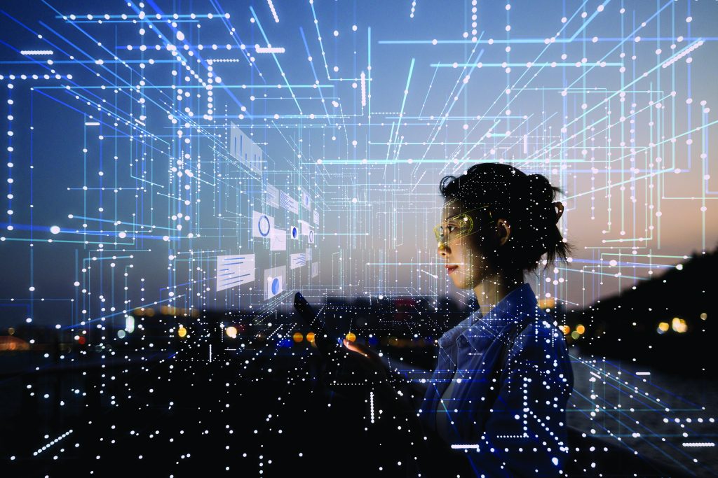 Person stands outdoors at dusk holding a device, surrounded by digital interface graphics with data charts and network lines overlaying the scene.