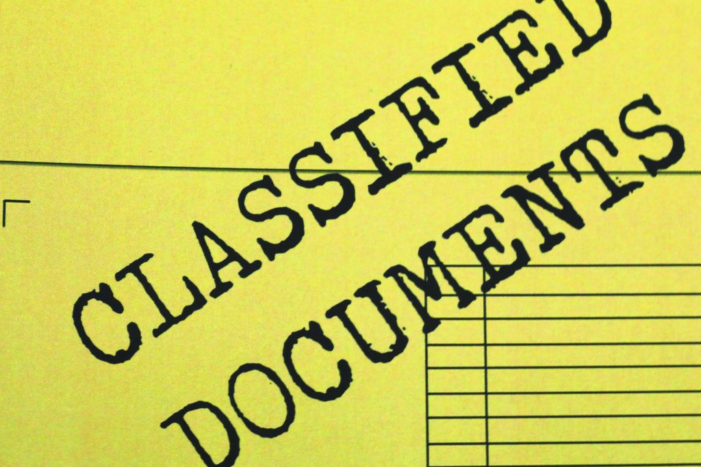 Close-up of a yellow document stamped ‘CLASSIFIED DOCUMENTS’ diagonally across the page, with form lines and margins visible beneath the bold lettering