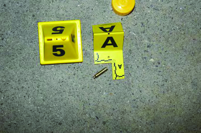 Yellow evidence markers labeled 5 and A placed on pavement beside a spent brass casing, showing crime scene documentation on a textured concrete surface