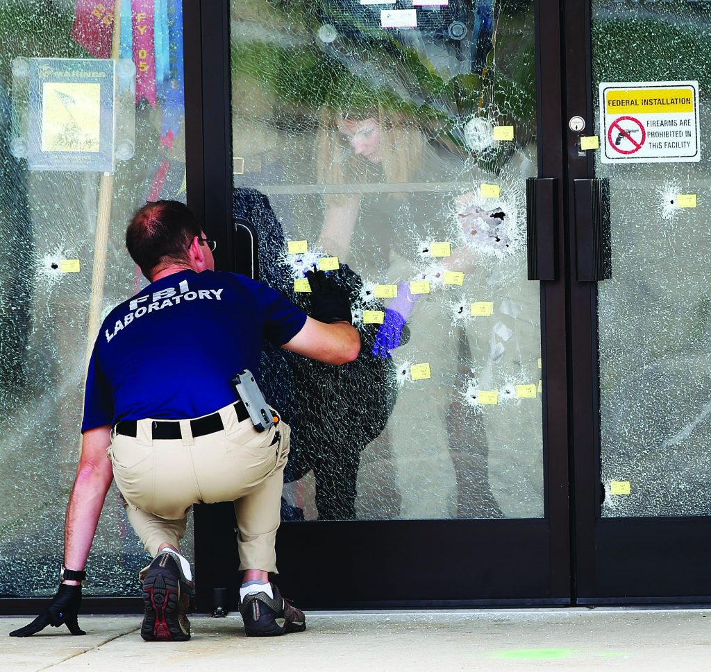 FBI laboratory examiner kneels inspecting shattered glass door marked with numerous bullet holes and evidence tags, with firearms sign posted