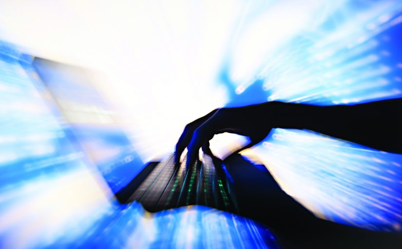 Silhouetted hands type on a laptop as bright light shines through the screen, with blue motion streaks forming a dynamic digital effect around it
