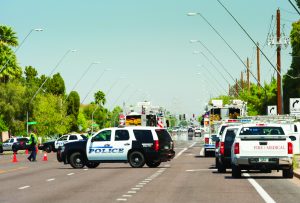 Police vehicles block palm-lined street; fire/EMS trucks on scene; officers manage traffic near power lines amid active emergency response.