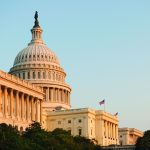 U.S. Capitol building with iconic dome and adjacent structures, lit by warm sunlight under clear sky; architectural details clearly visible