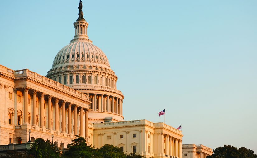 U.S. Capitol building with iconic dome and adjacent structures, lit by warm sunlight under clear sky; architectural details clearly visible