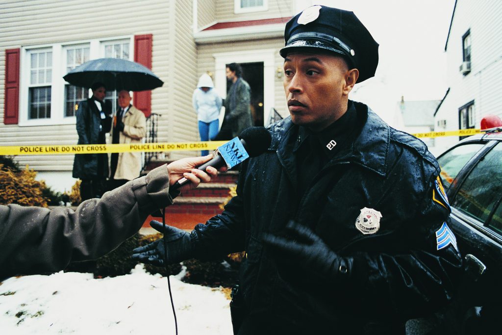 Policeman Being Interviewed by the Media on a Driveway at a Crime Scene
