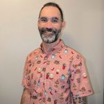 Individual in pink short-sleeve shirt with taco, chili, and drink illustrations; visible tattoos on left arm